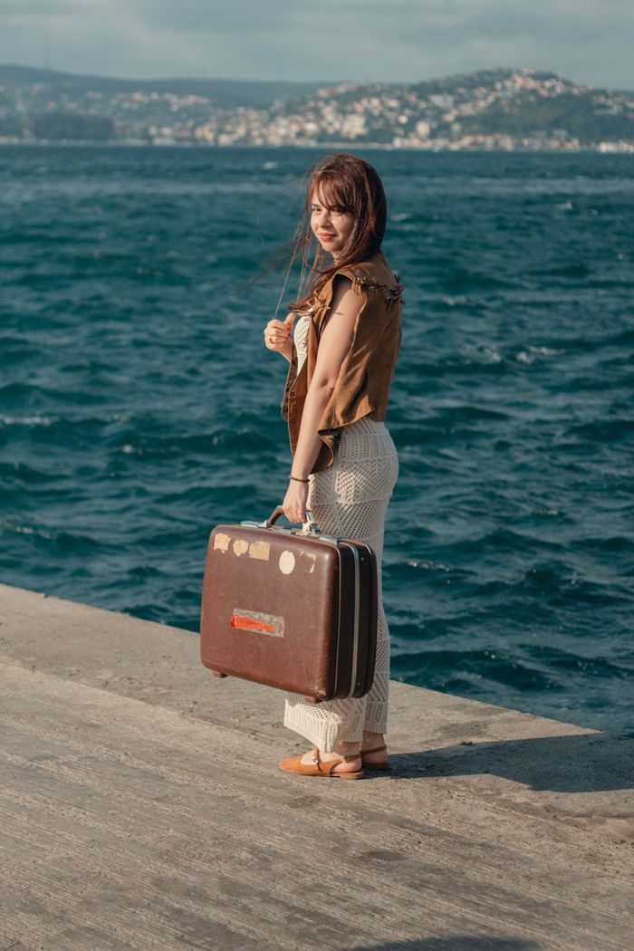 A woman holds a vintage suitcase by the sea in Istanbul, capturing a moment of travel and exploration.