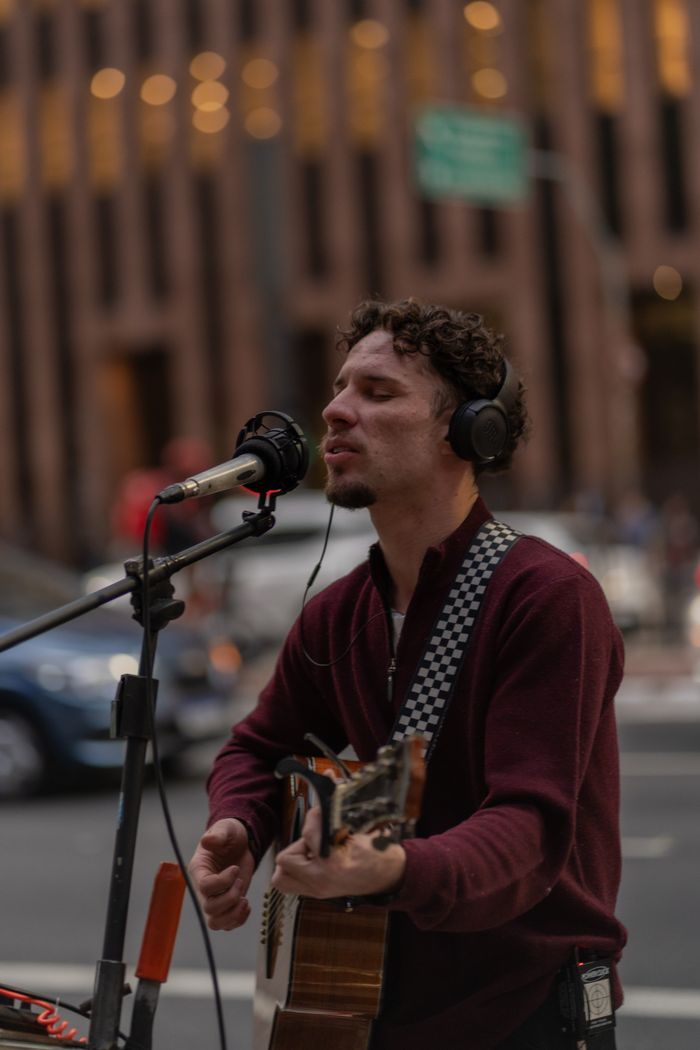 Musician performing live with guitar and microphone on an urban street.