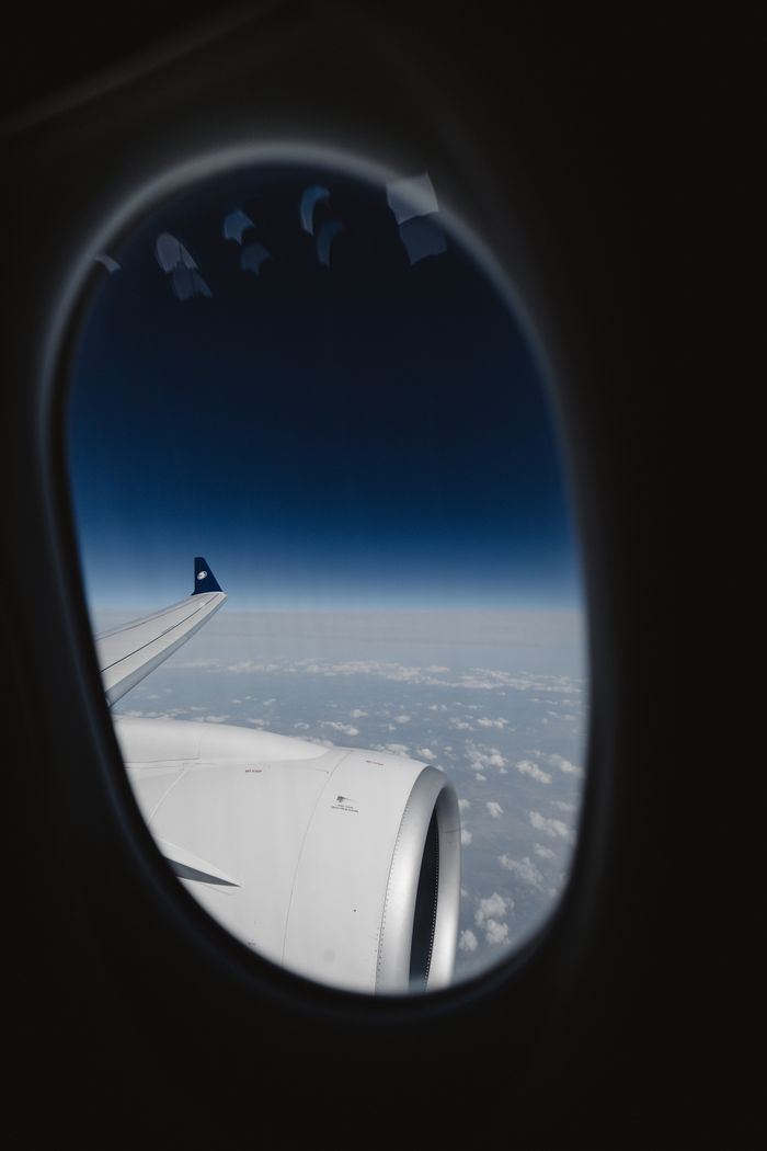 Scenic aerial view from airplane window showing sky and clouds with wing in focus.