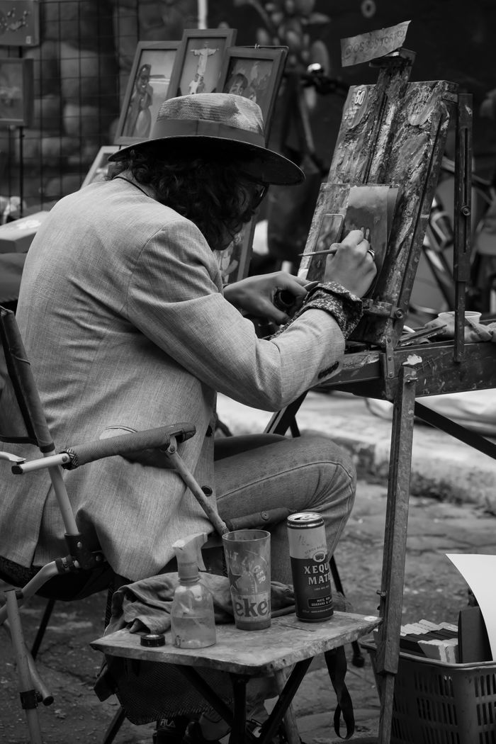 Black and white street photography of an artist painting outdoors, showcasing creativity.