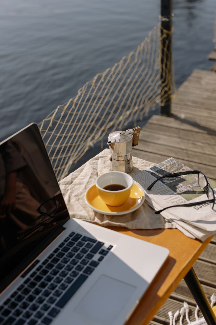 Relaxing outdoor workspace setup by the lake with coffee and laptop, perfect for inspiration.