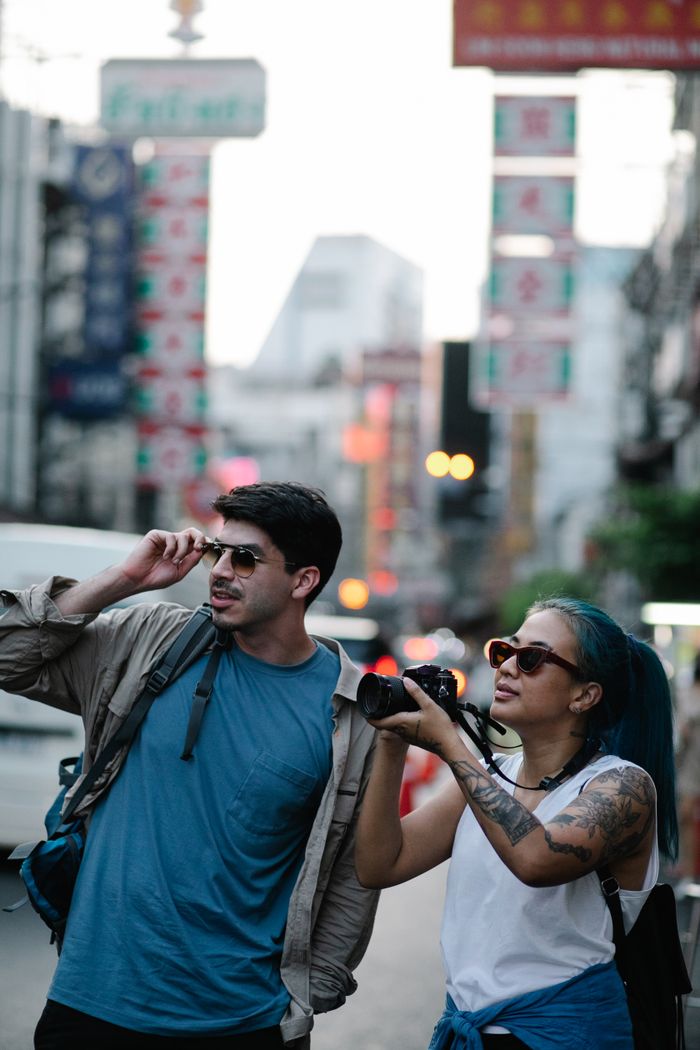 Two stylish travelers explore the bustling city streets, capturing moments with a camera.