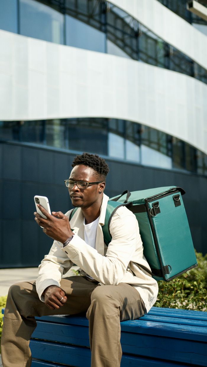 menu-02 Modern food delivery person using smartphone while sitting on a city bench.